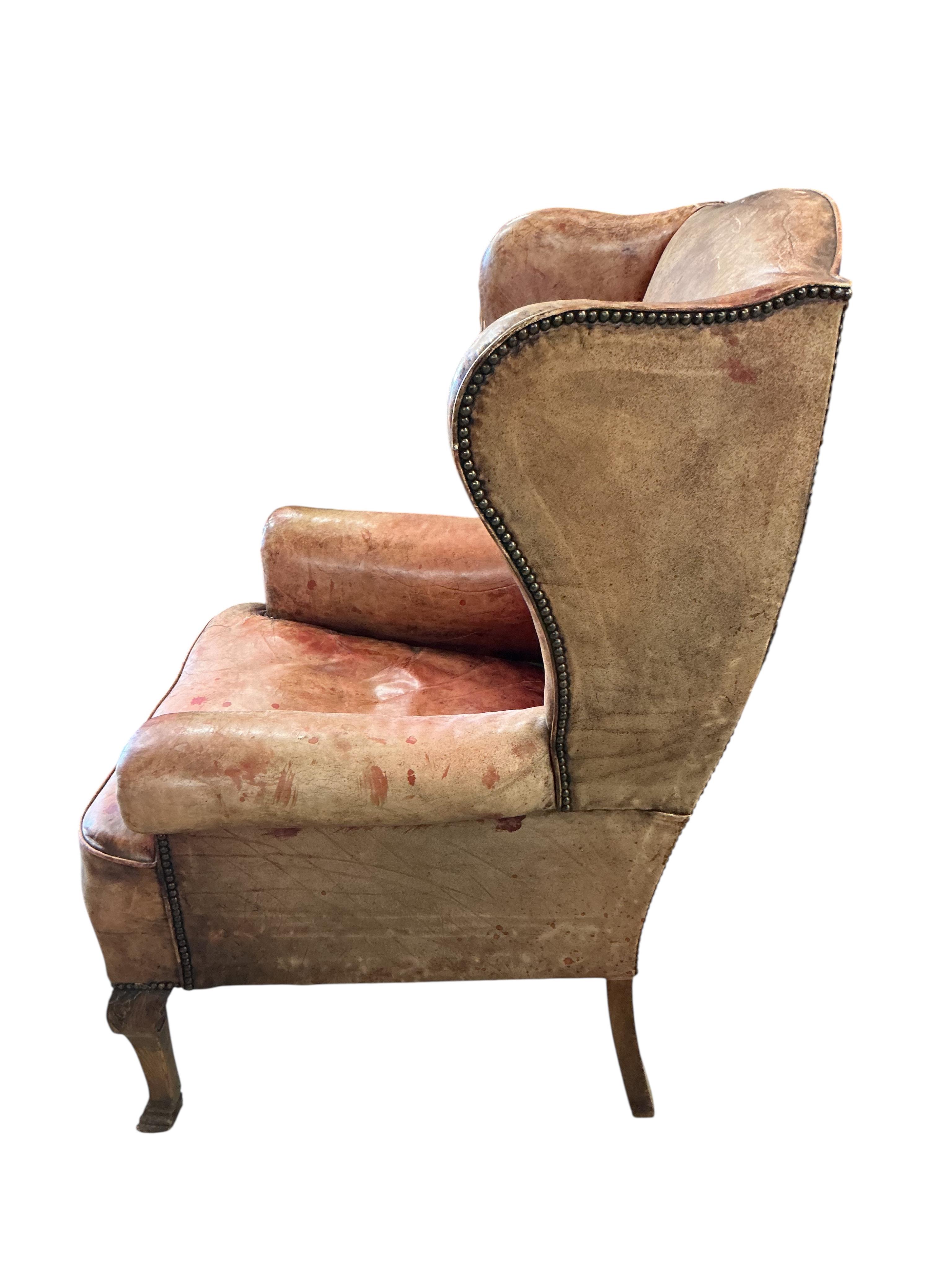 A George III style studded pale red leather wing armchair on carved oak cabriole legs, width 74cm, depth 78cm, height 110cm